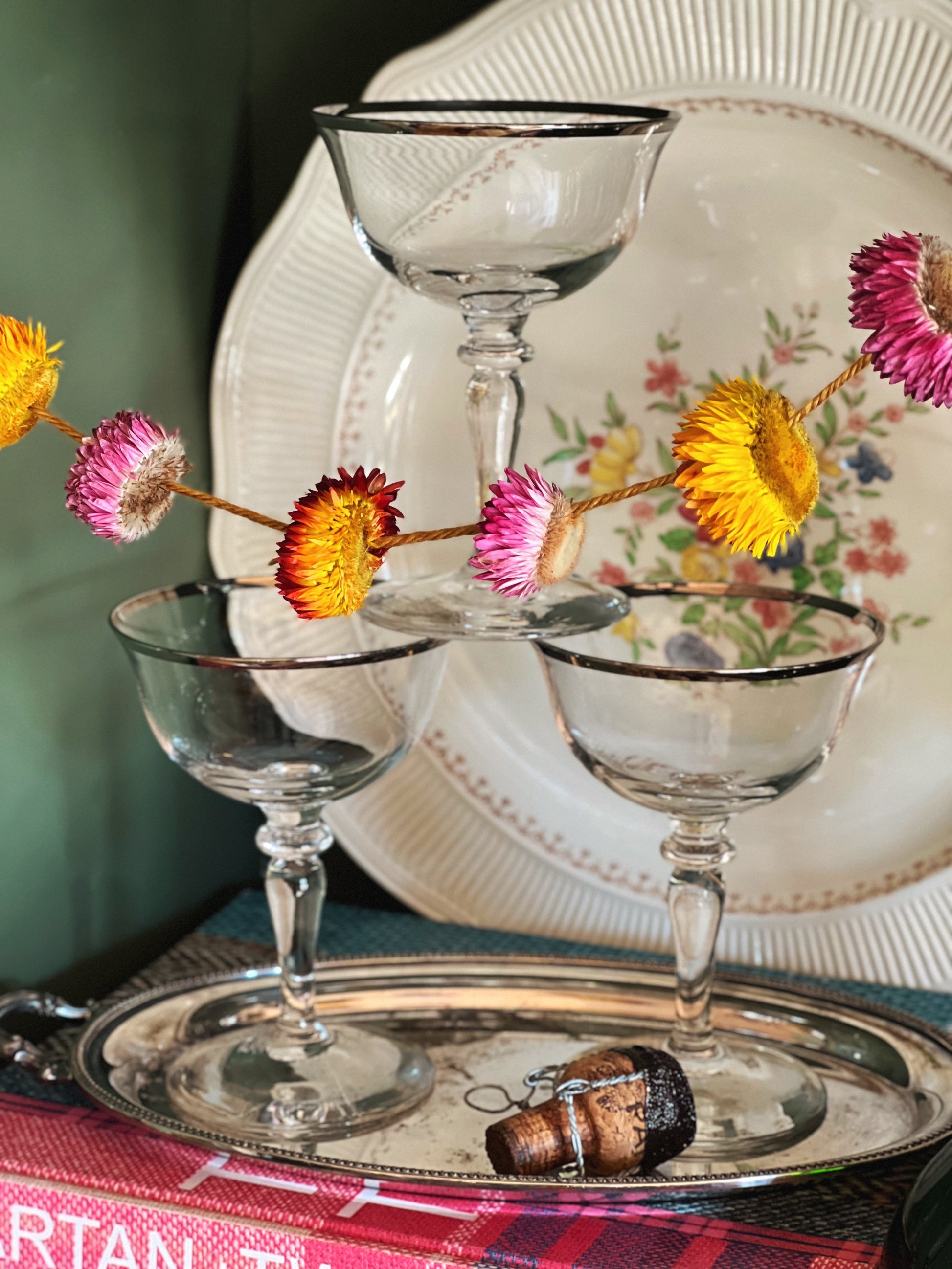 Decorative setting with glassware, flowers, and a silver tray on a table.