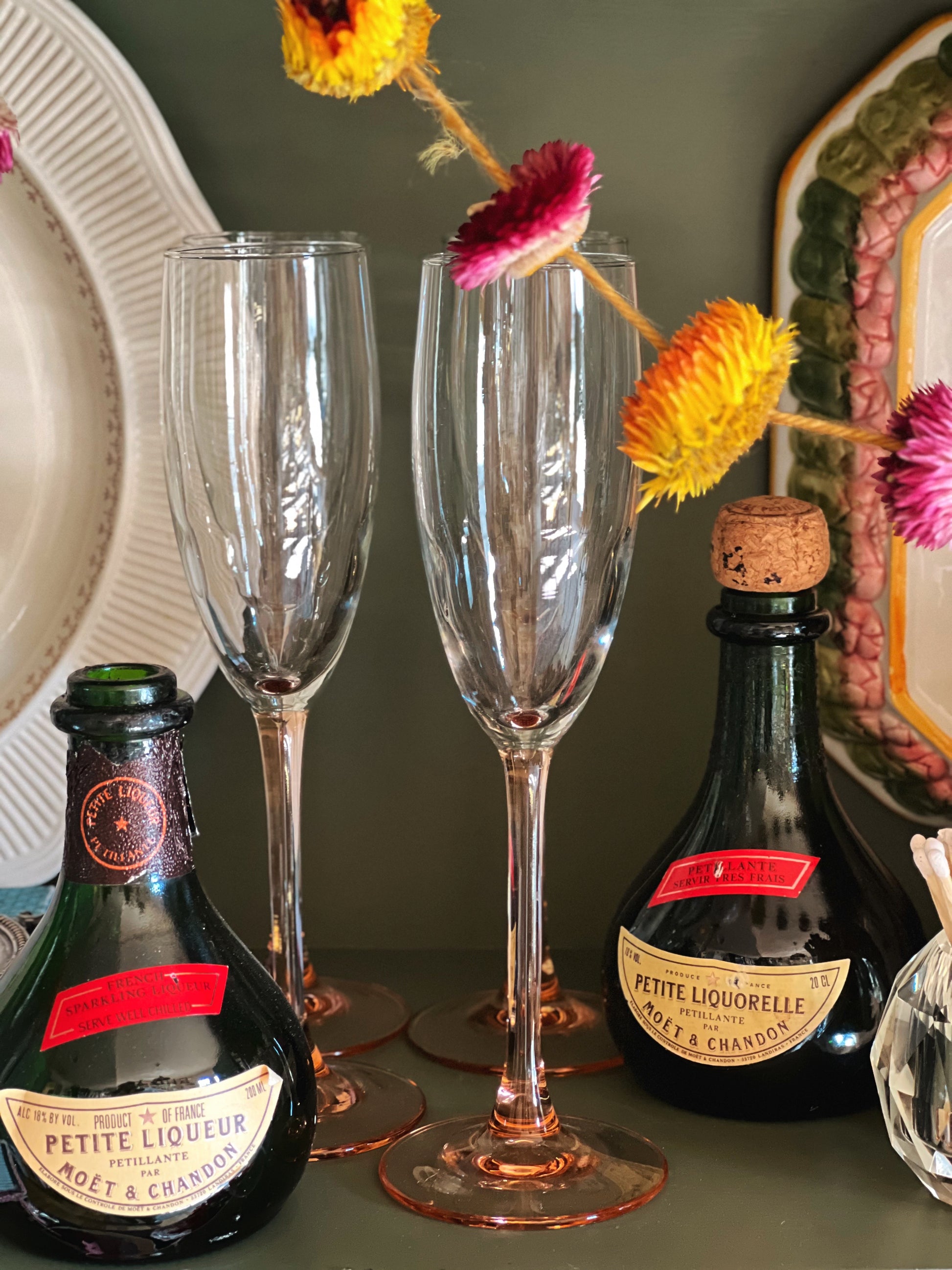 Two champagne flutes with bottles of Petite Liquorello on a decorative table.
