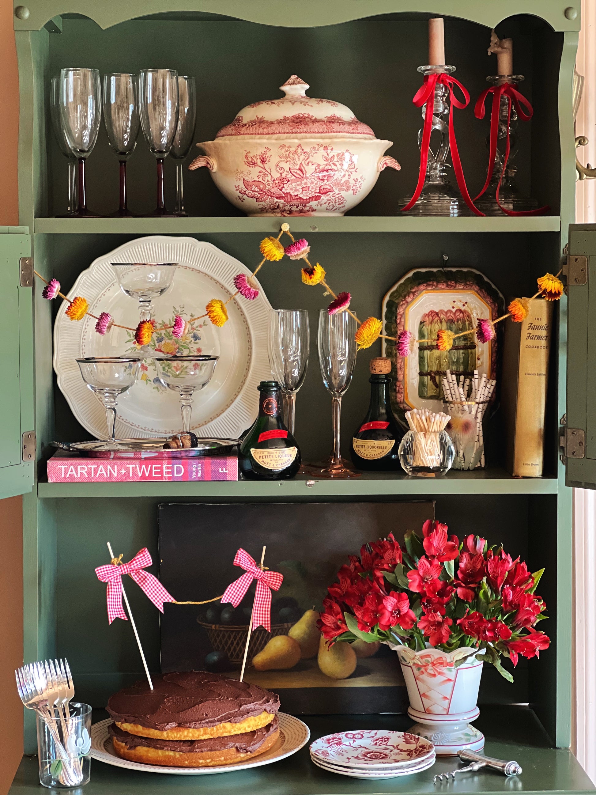 Decorative shelf with various items including glasses, a cake, and flowers.