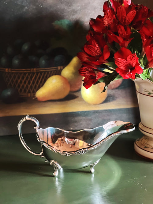 Silver gravy boat with red flowers and pears in the background