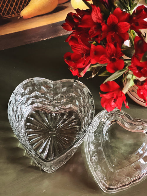 Heart-shaped glass containers on a reflective surface with red flowers in the background