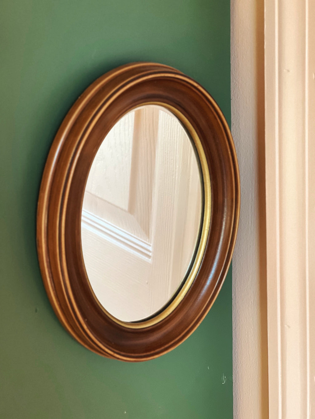 Round wooden-framed mirror on a green wall