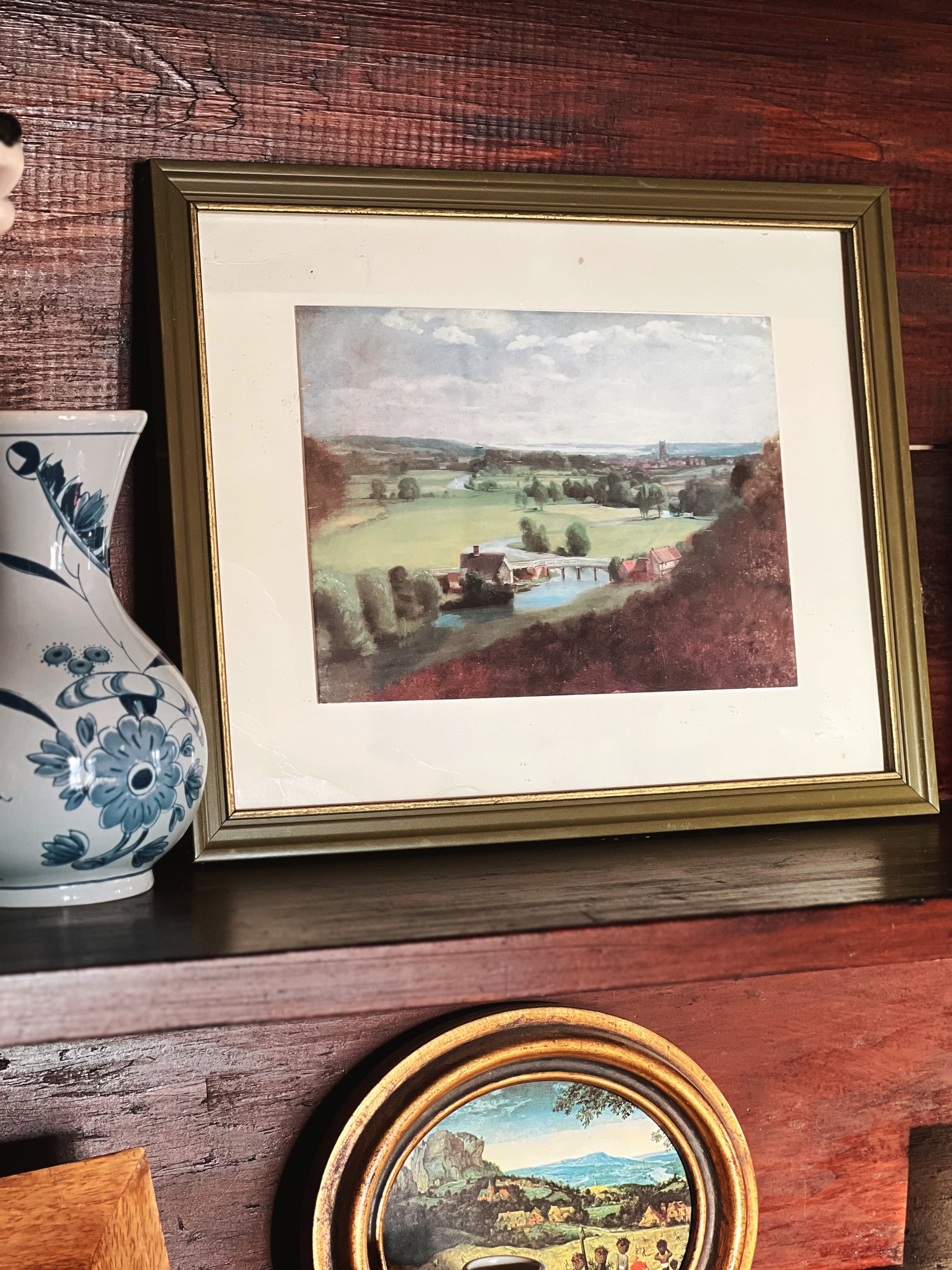 Framed landscape painting on a wooden surface with a decorative vase.