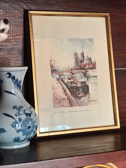 Framed artwork of a cityscape with a decorative vase on a wooden surface