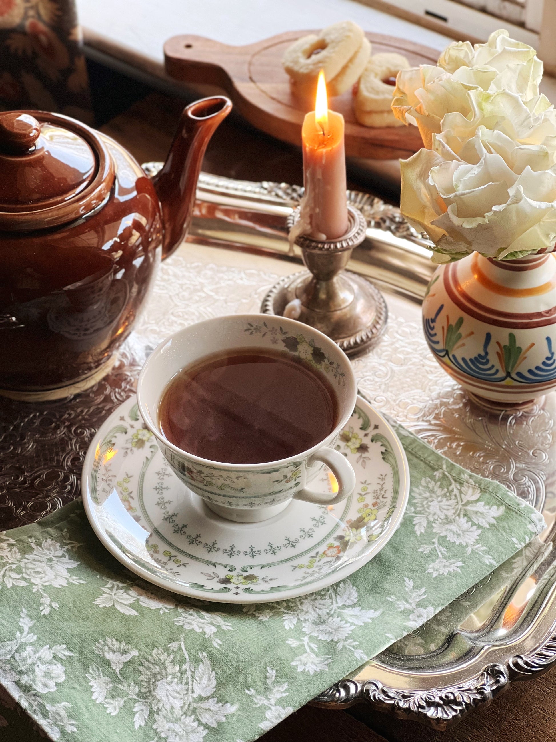 Tea set with a teapot, cup, and saucer on a table with a candle and flowers.