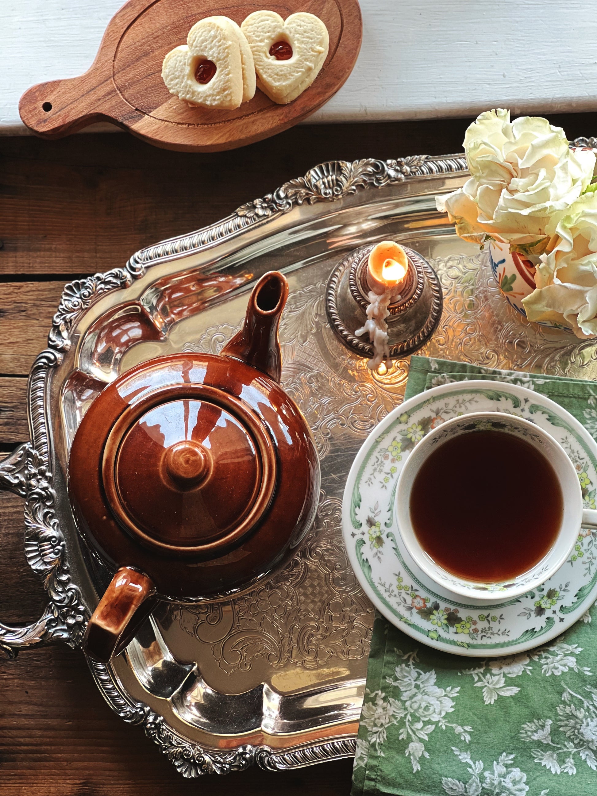 Tea set with teapot, cup, and cookies on a decorative tray.