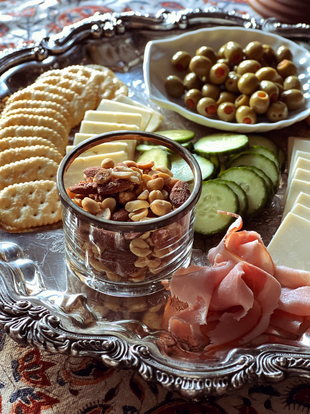 Platter with assorted snacks including crackers, cheese, olives, and cured meats on a decorative tray.