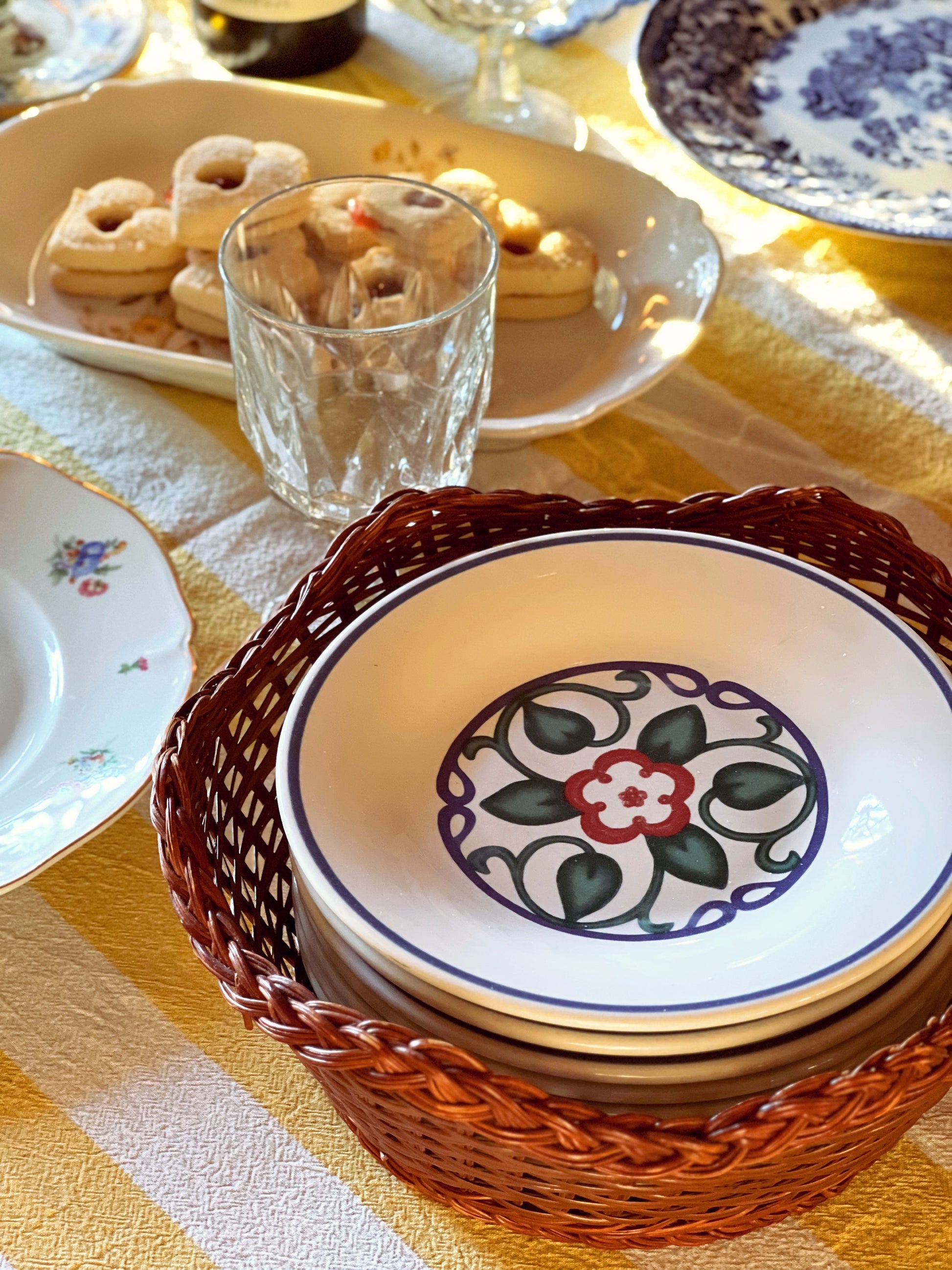 Stack of decorative ceramic plates in a wicker basket on a table with a yellow tablecloth.