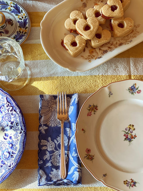 Dining table setting with heart-shaped cookies, plates, and cutlery on a striped tablecloth.