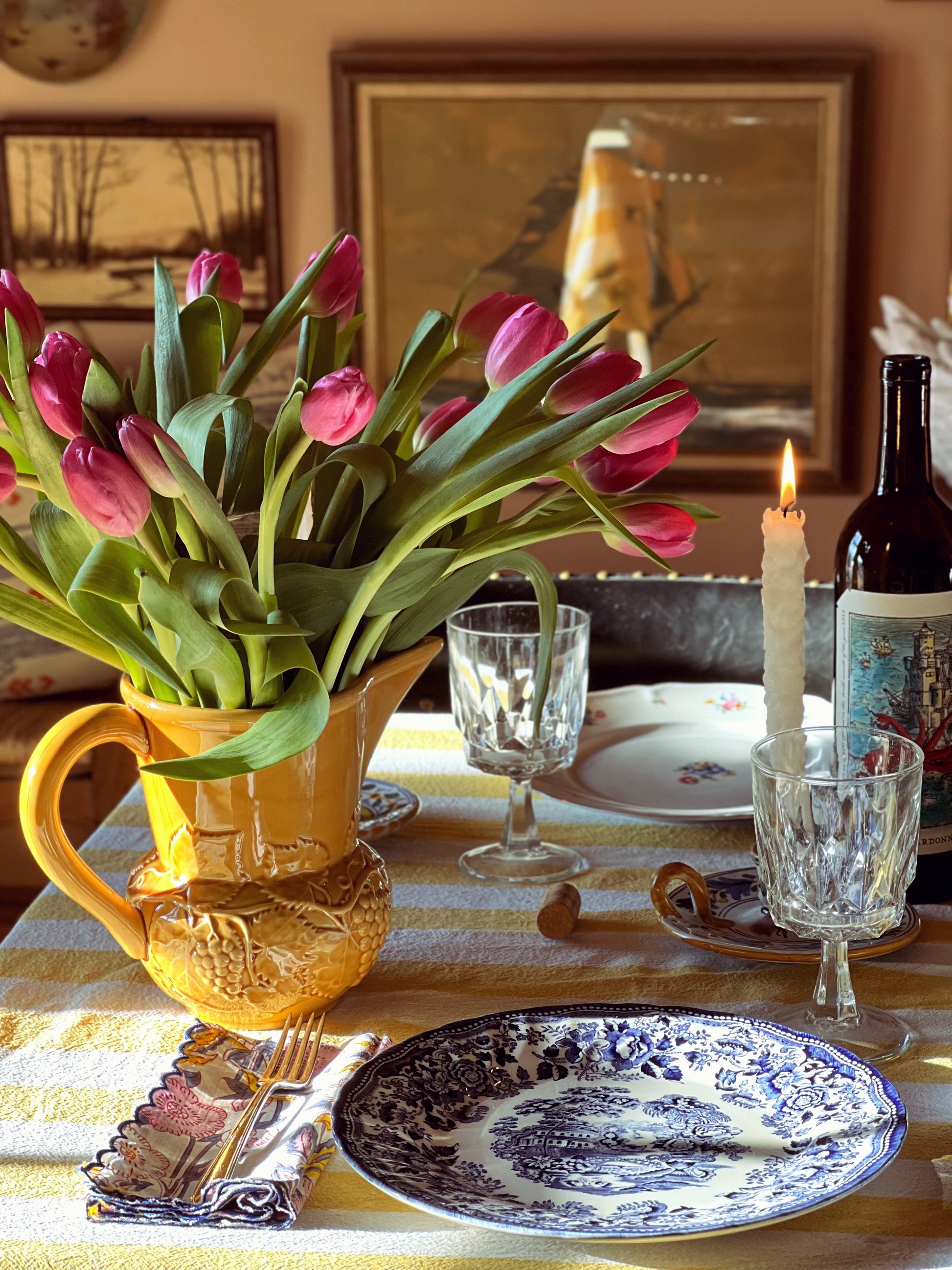 Dining table setting with tulips, plates, glasses, and a candle.