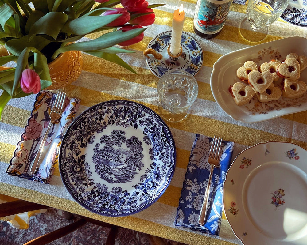Dining table set with plates, glasses, and a bottle of beer on a yellow tablecloth.