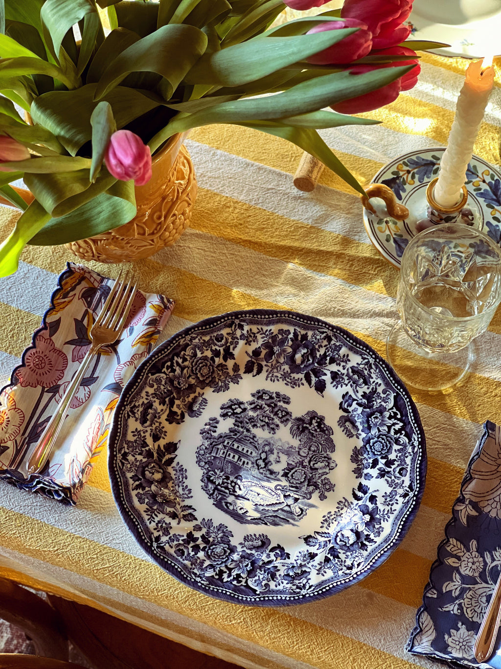 Decorative table setting with a blue and white plate, pink tulips, and yellow tablecloth.
