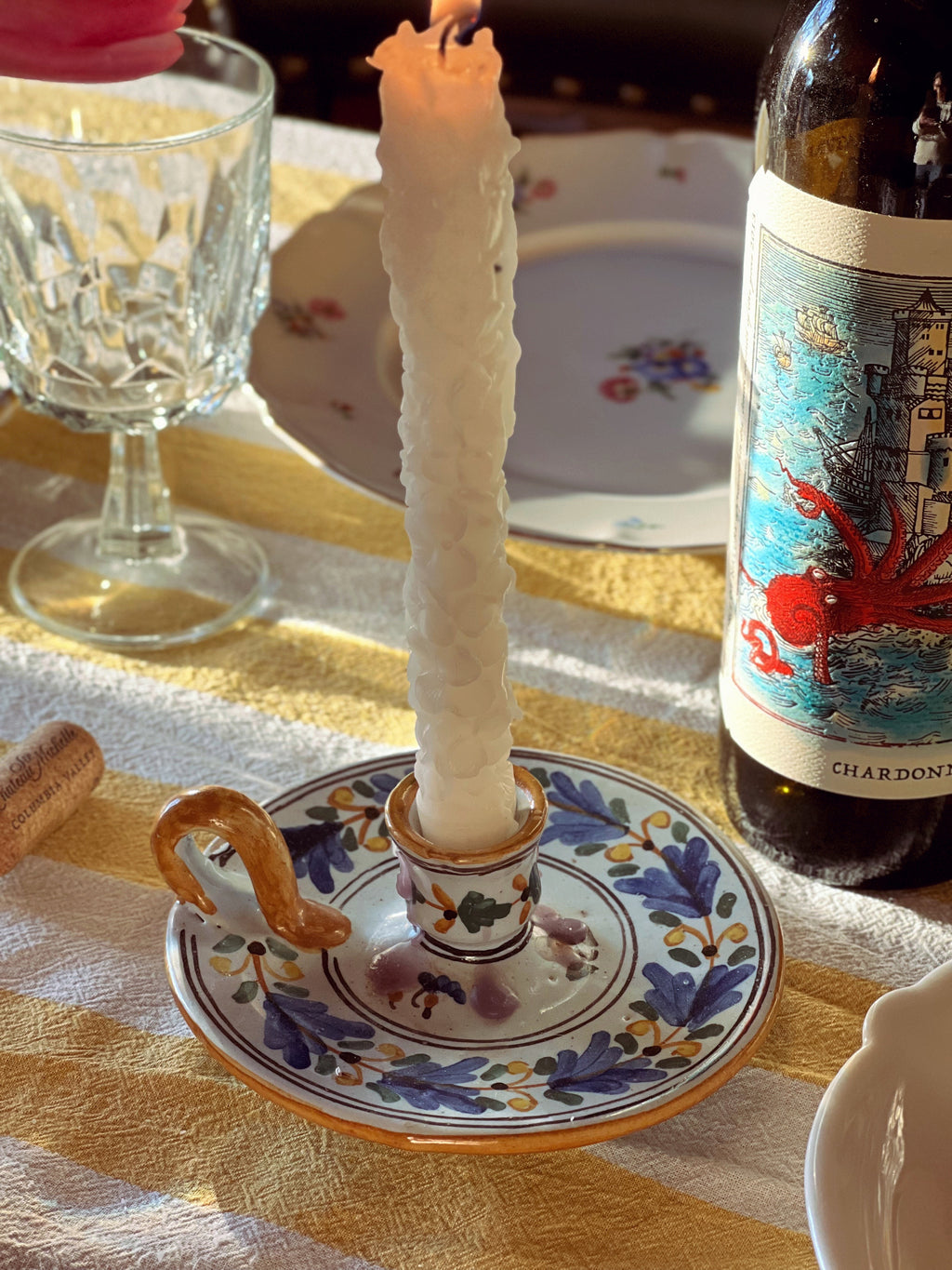 Candle in a decorative holder on a table with a bottle of Chardonnay and glasses.