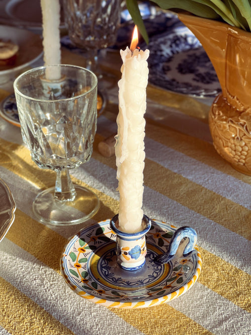 Candle in a decorative holder on a table with a glass and a striped tablecloth.
