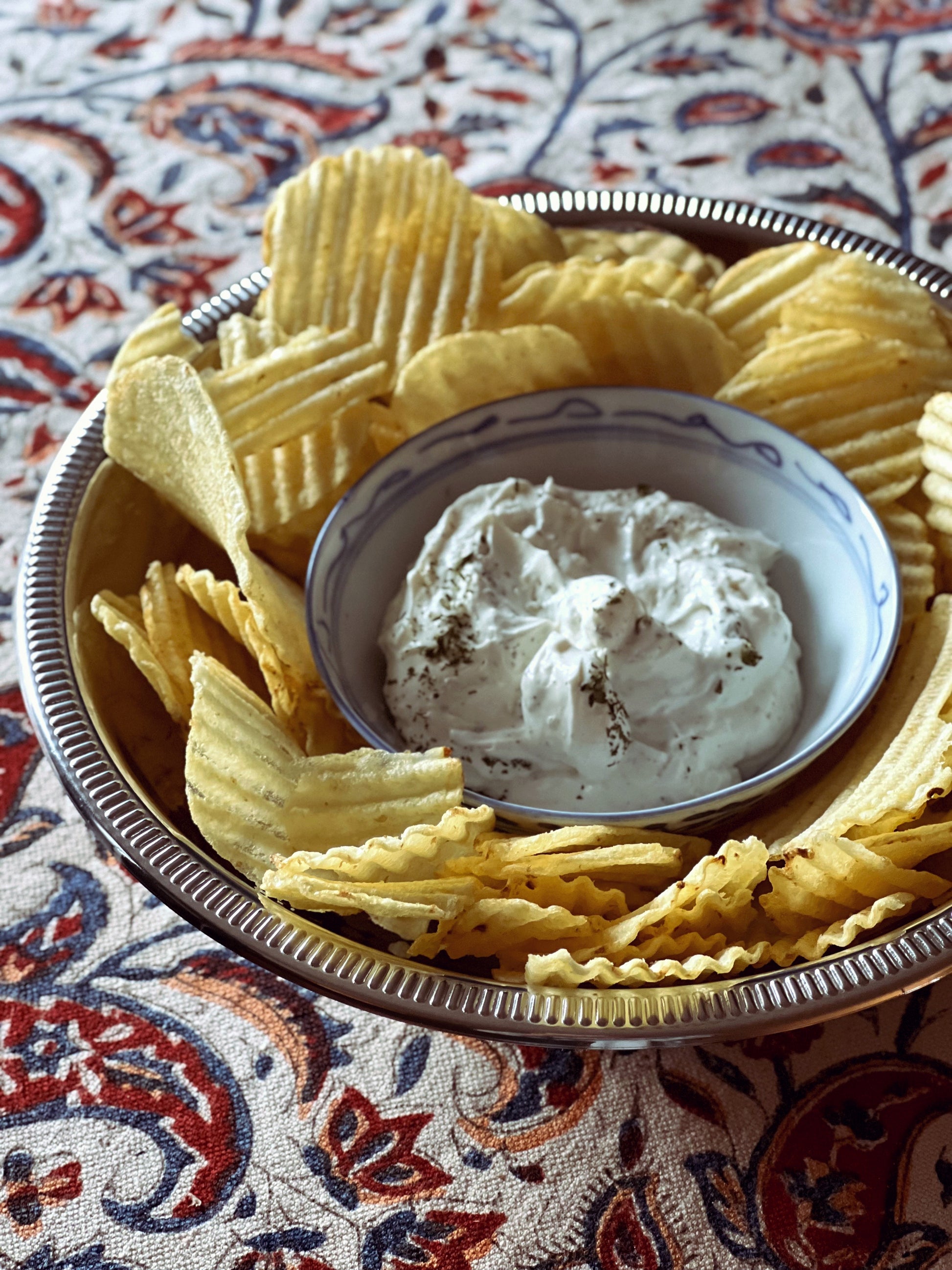 Bowl of potato chips with a small bowl of dip on a patterned fabric background