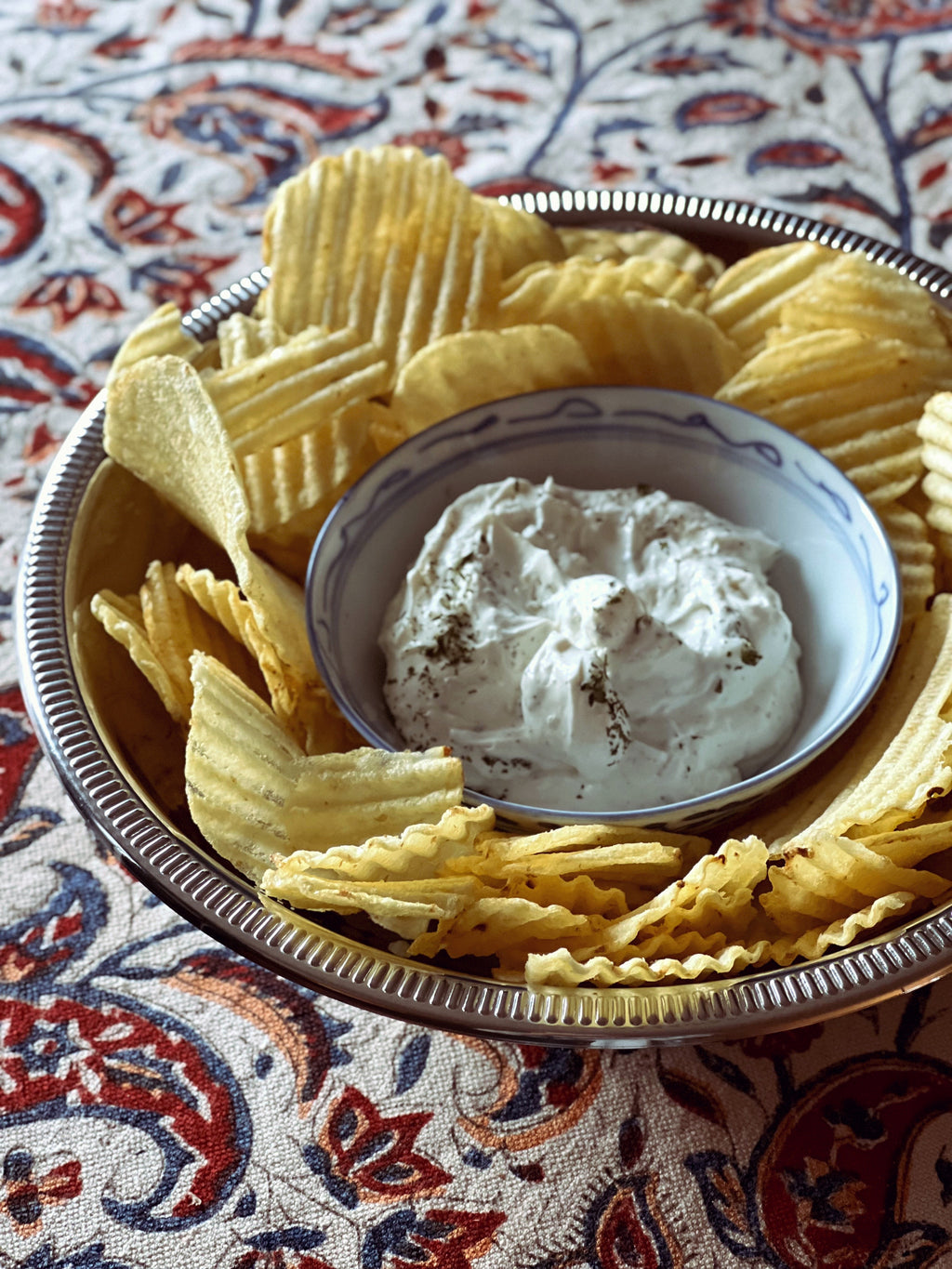 Bowl of potato chips with a small bowl of dip on a patterned fabric background