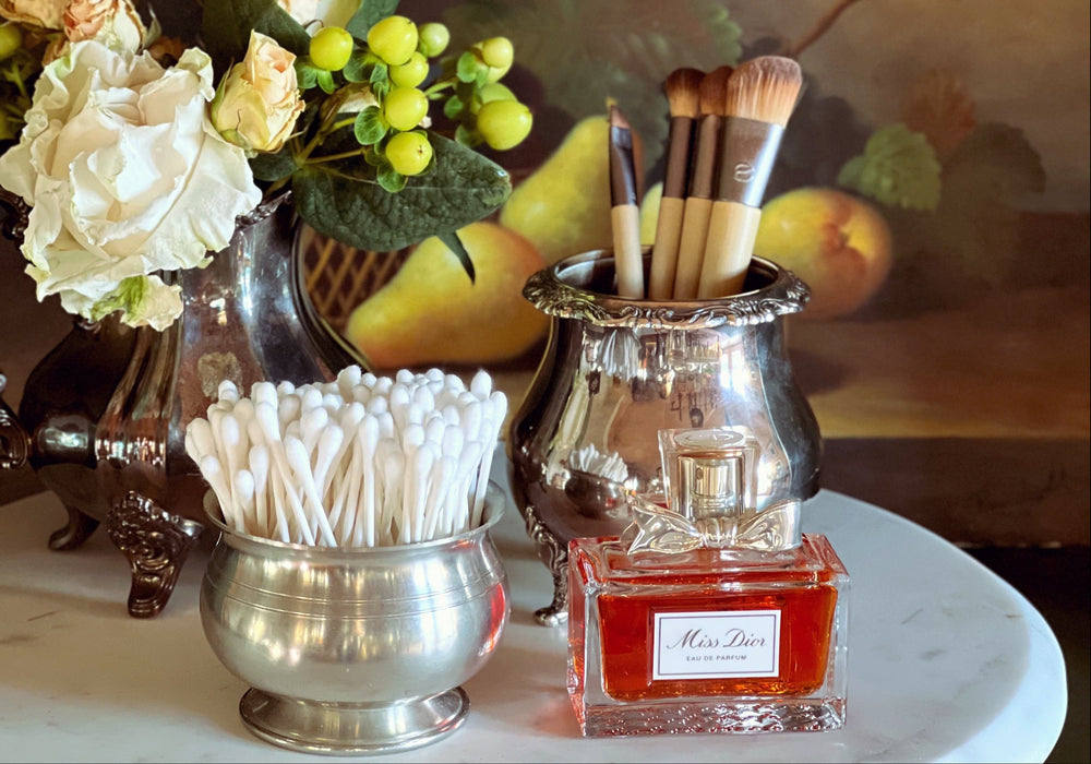 Decorative still life with silver containers, flowers, and a perfume bottle on a marble surface.
