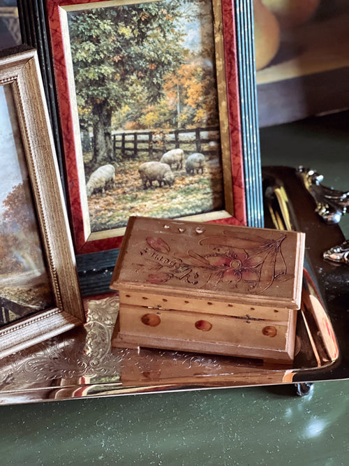 Wooden box with intricate carvings on a reflective surface, with framed pictures of sheep in the background.