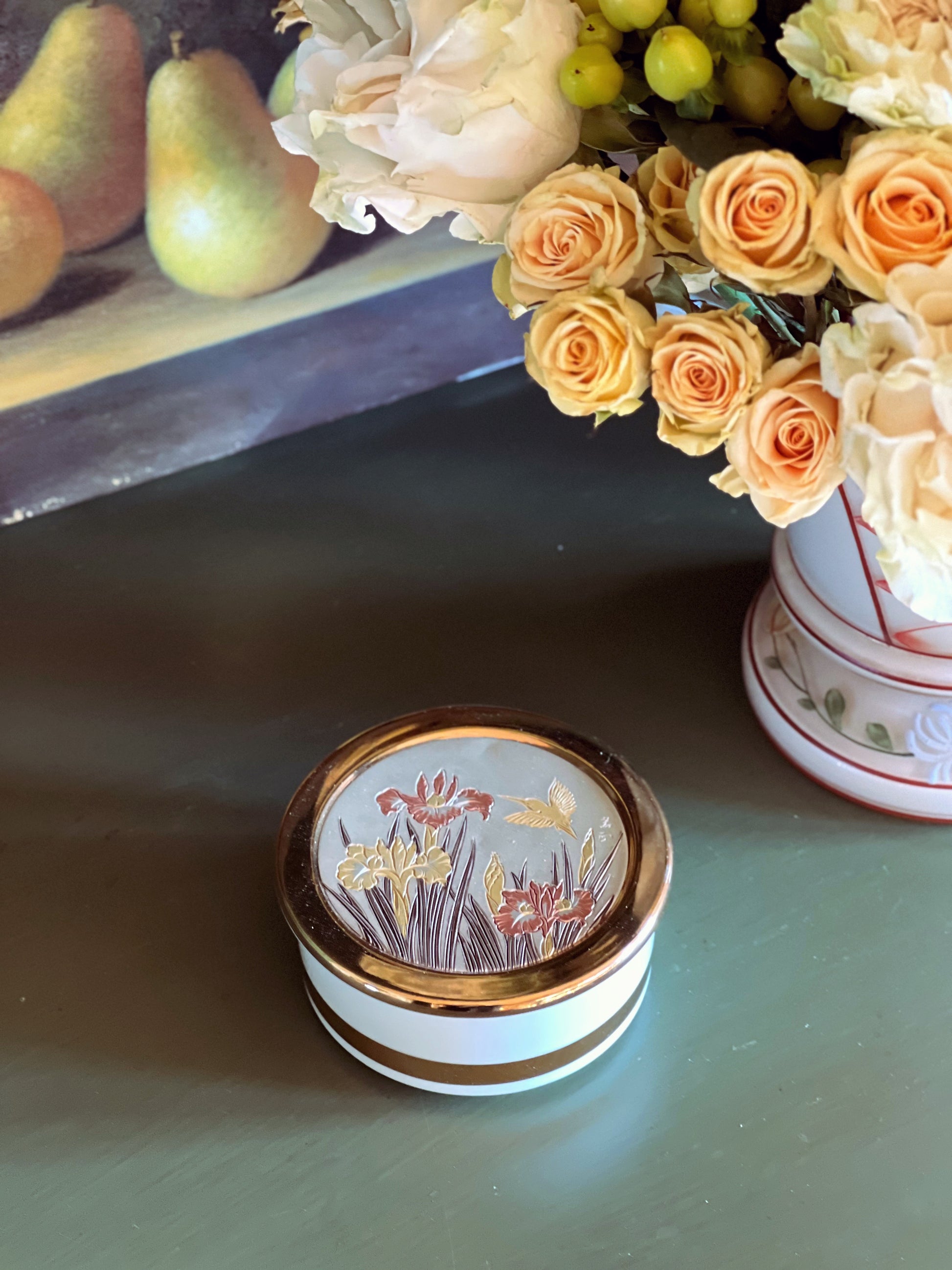 Decorative box with floral design on a table with flowers and fruit in the background