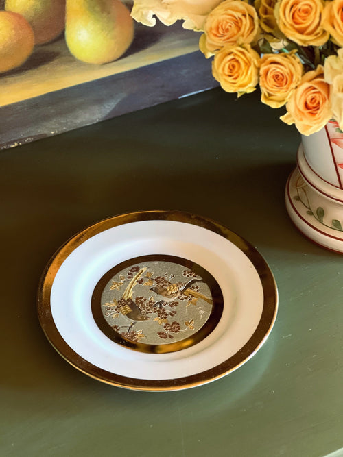 Decorative plate with intricate design on a green surface, with flowers and apples in the background.