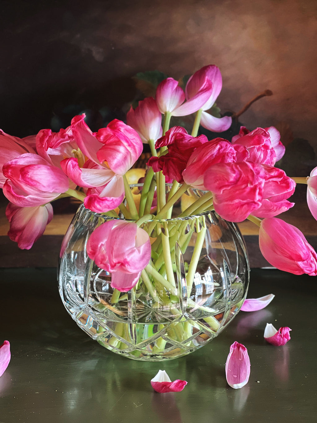 Clear glass vase with pink flowers on a reflective surface