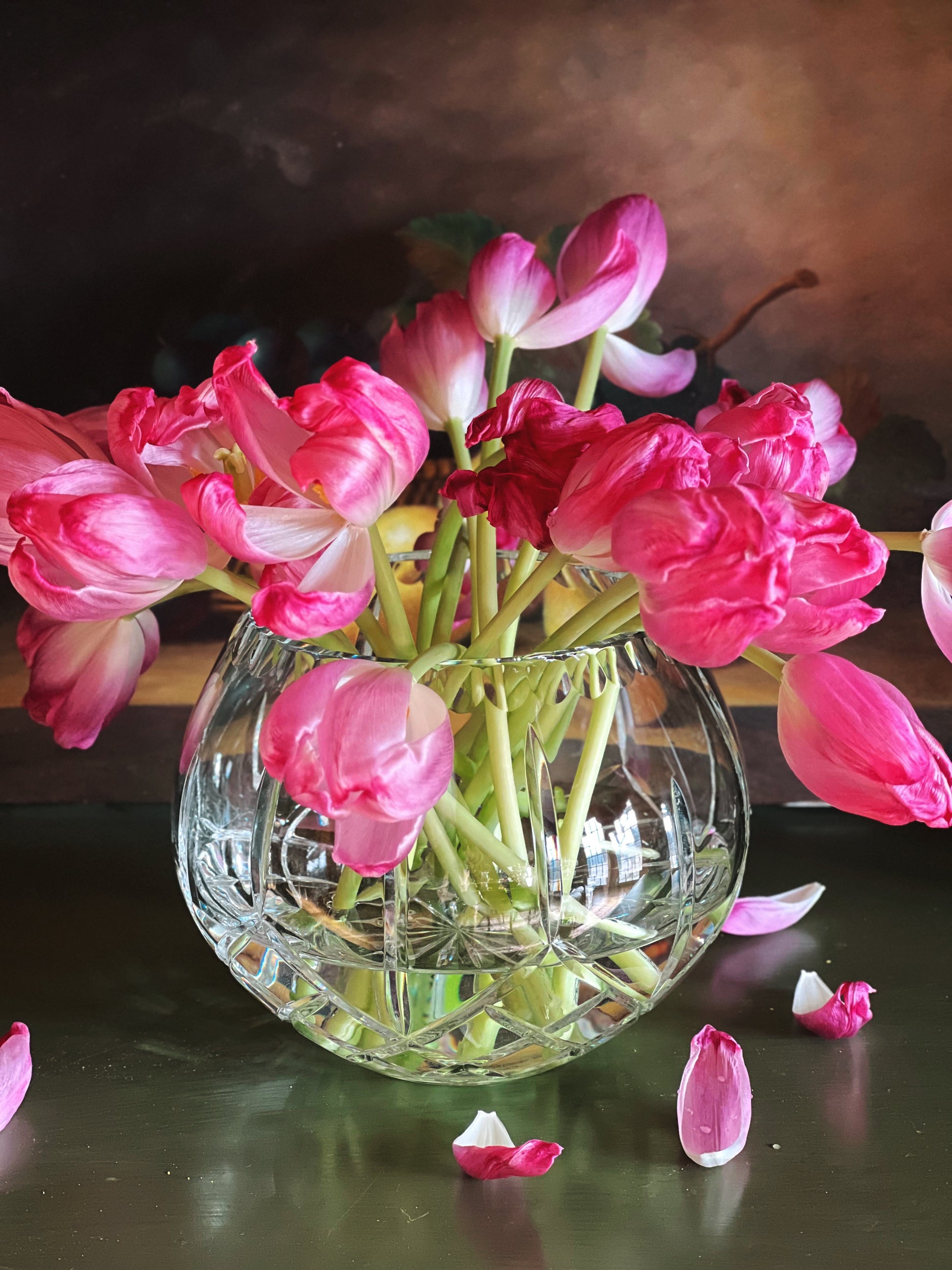 Clear glass vase with pink flowers on a reflective surface
