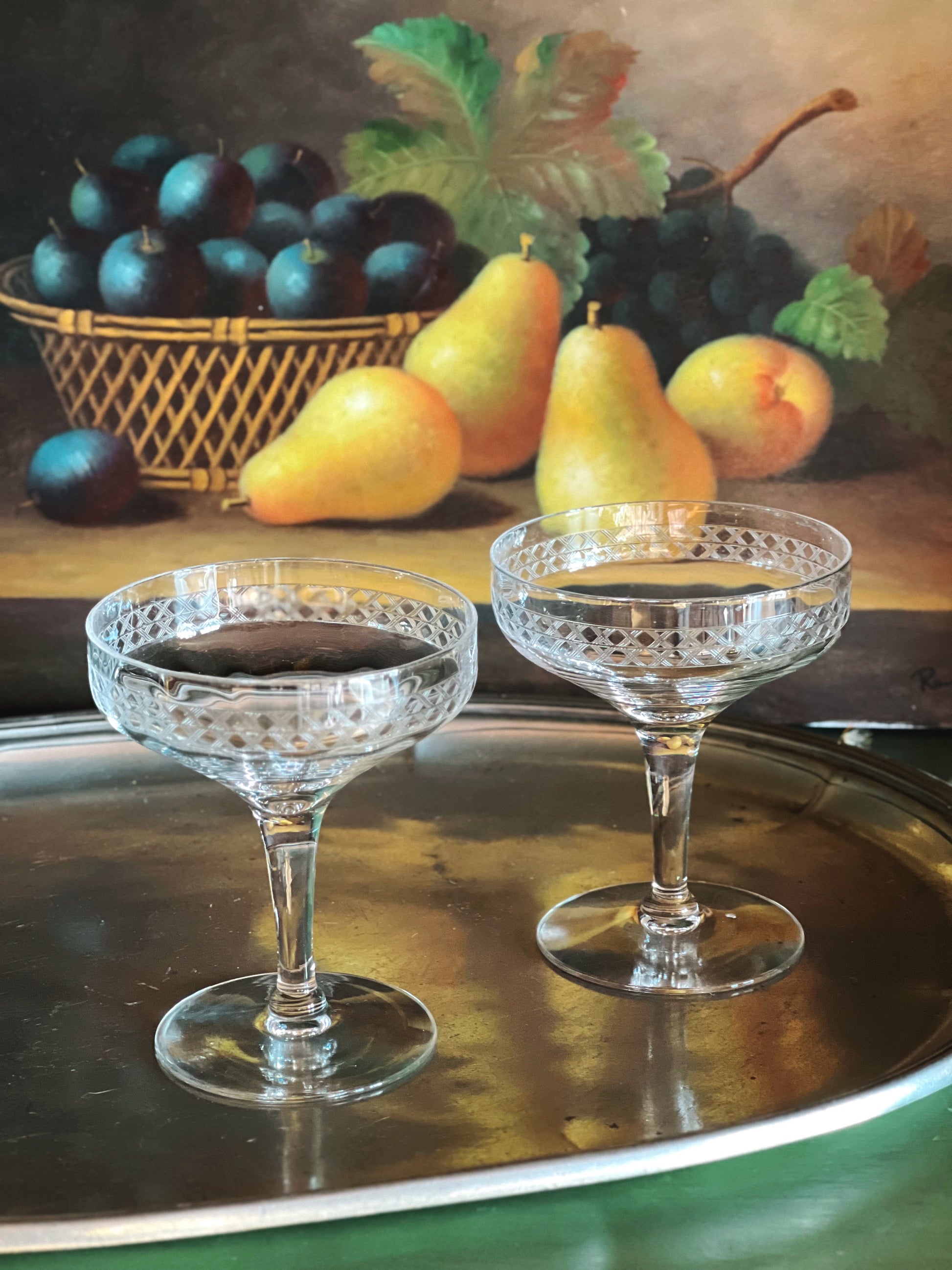Two crystal glasses on a metal tray with plums and pears in the background