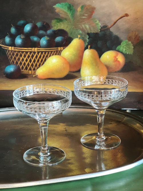 Two crystal glasses on a metal tray with plums and pears in the background