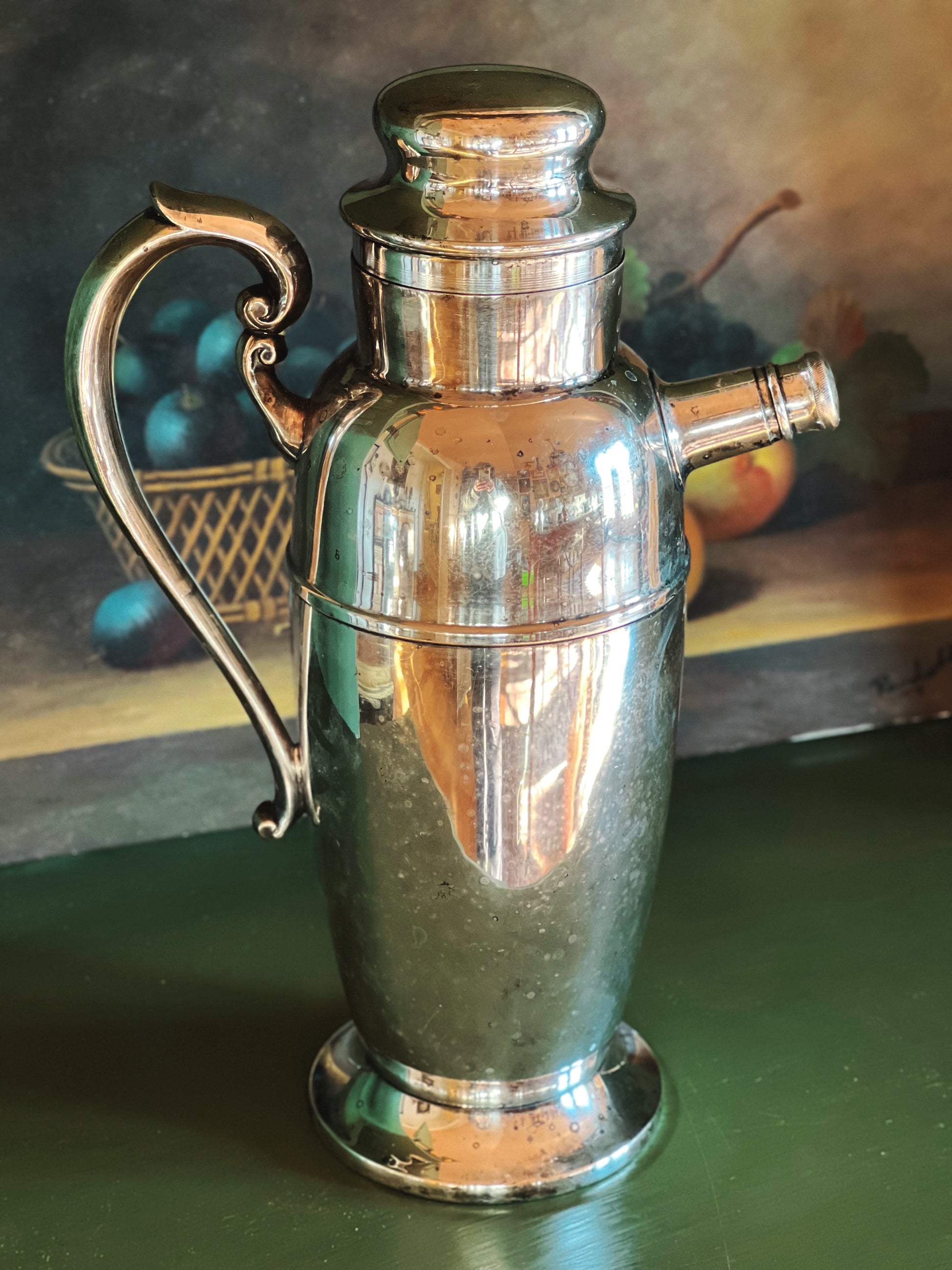 Silver pitcher with decorative handle on a green surface