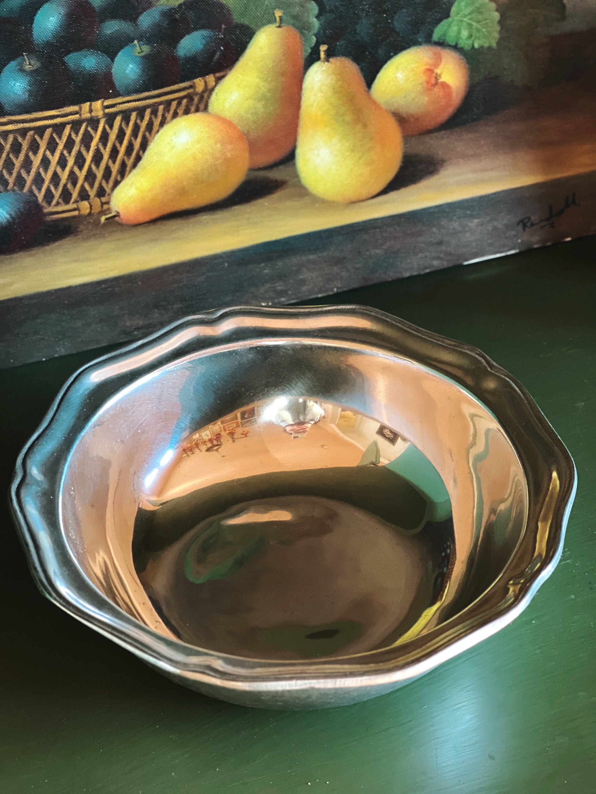 Silver bowl on a green surface with fruit in the background