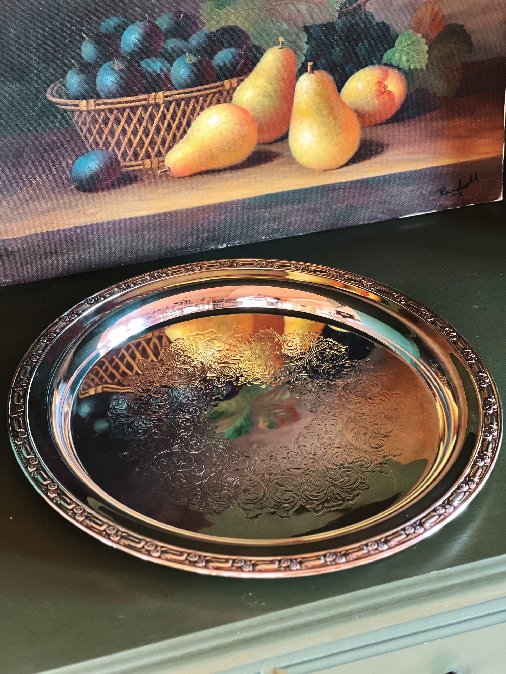Decorative silver tray with a still life painting of fruit in the background