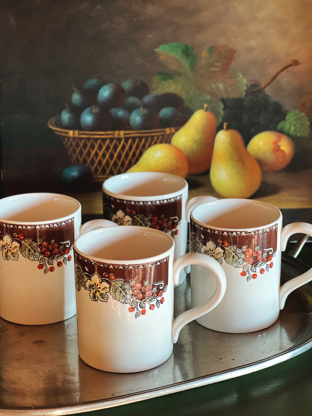 Four Gibson stoneware mugs with decorative handles on a table with fruit in the background