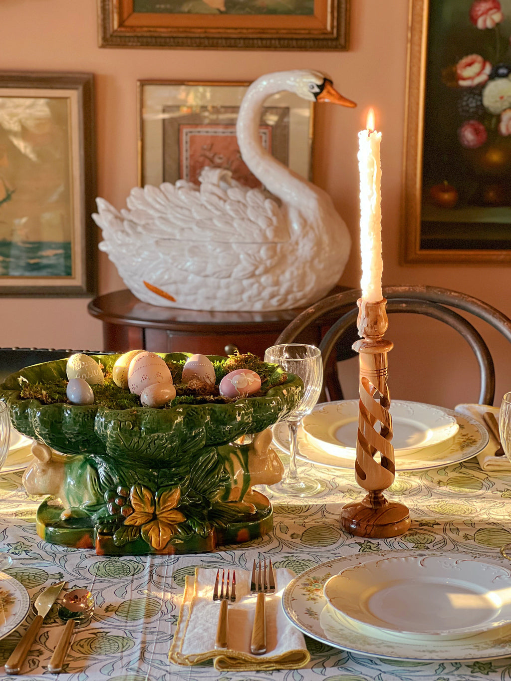 Decorative table setting with a green glass bowl, candle, and swan sculpture.