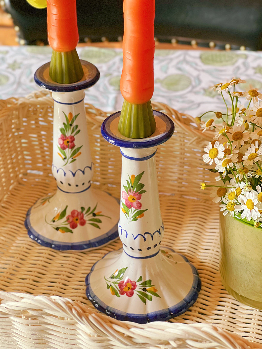 Decorative candle holders with floral designs on a woven surface.
