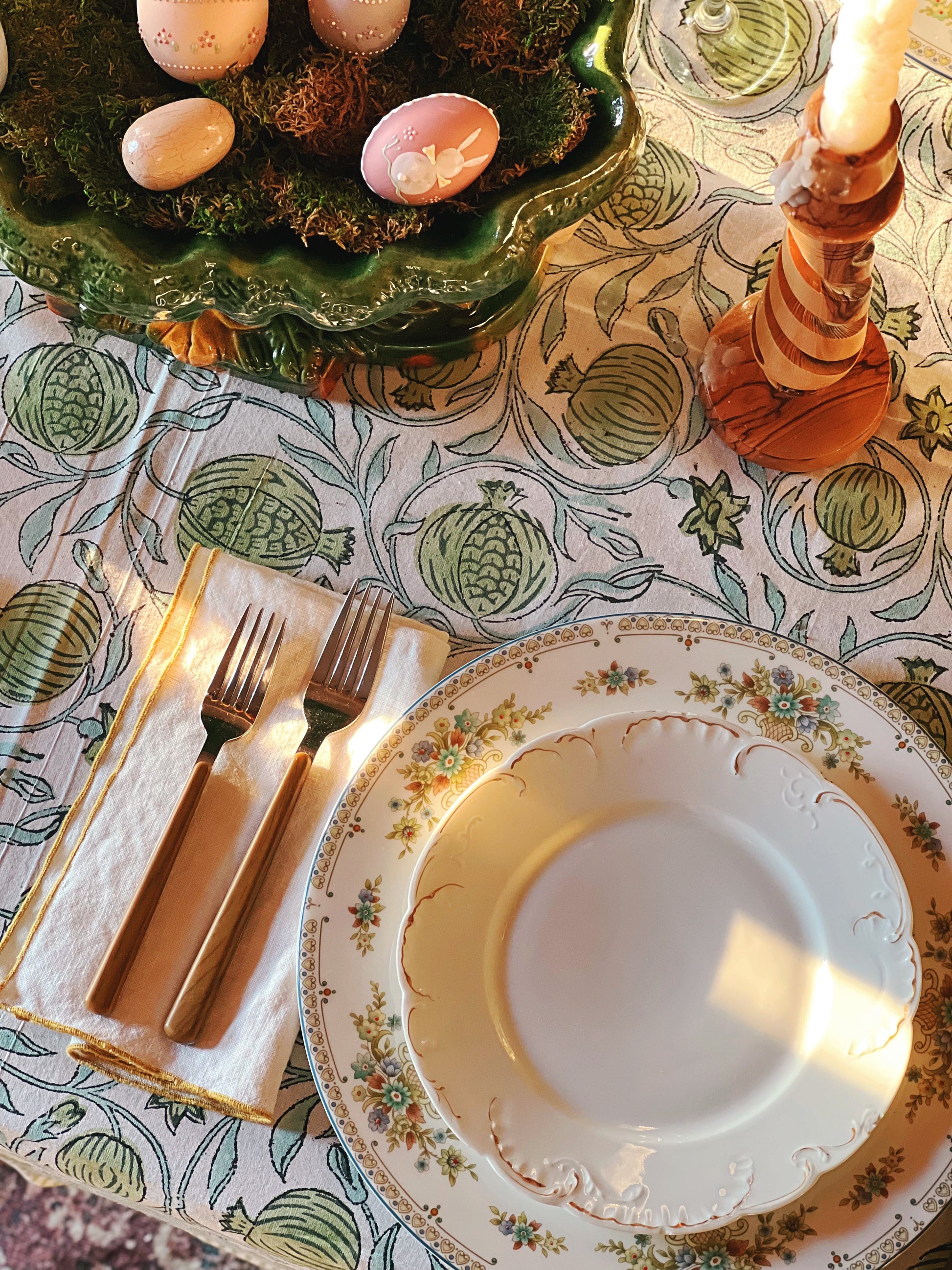 Dinner table setting with floral plates, cutlery, and a candle on a patterned tablecloth.