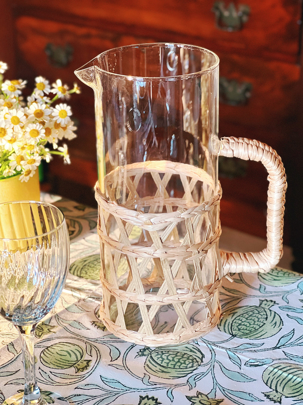 Clear glass pitcher with wicker handle on a patterned tablecloth