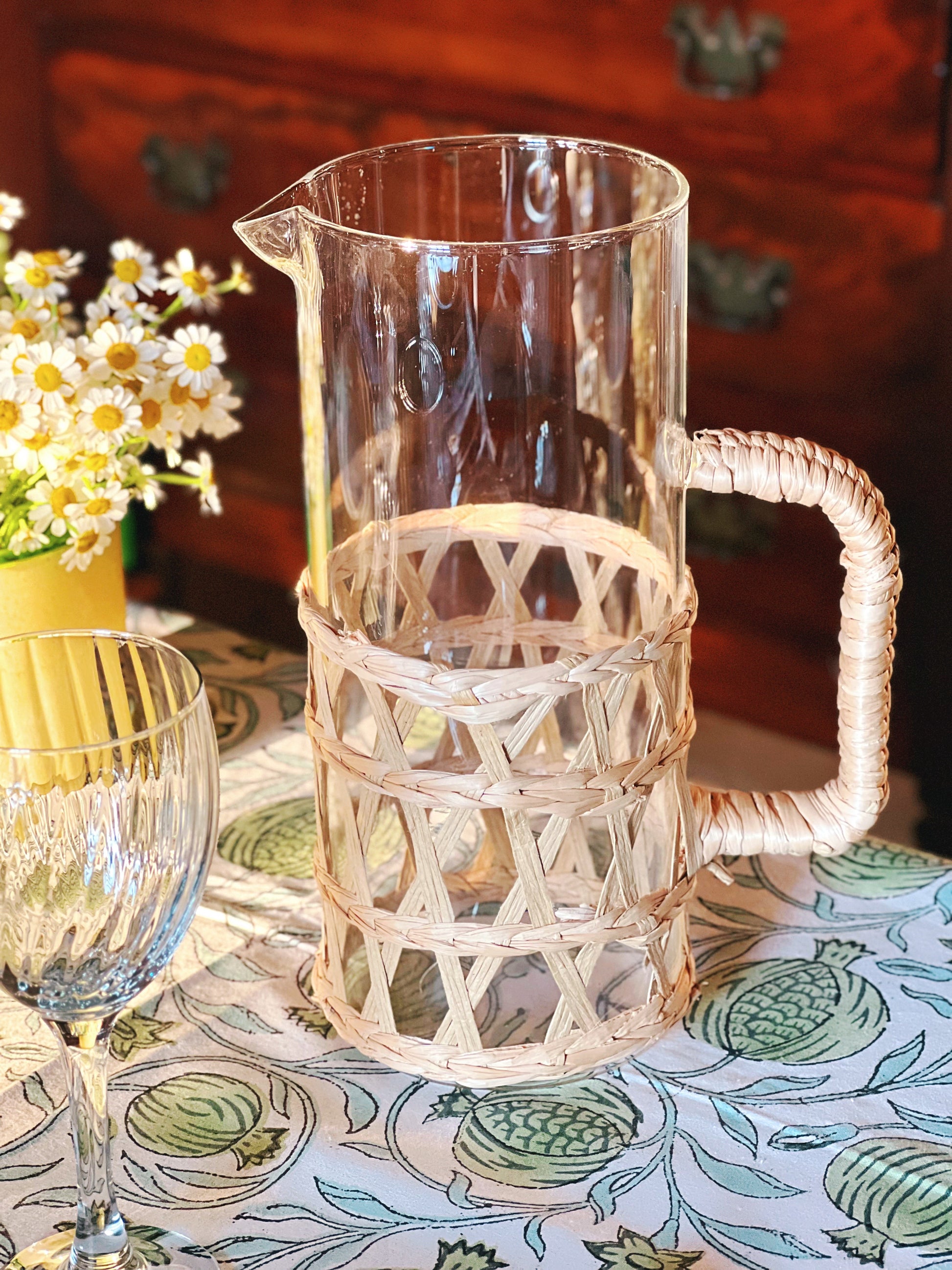 Clear glass pitcher with wicker handle on a patterned tablecloth