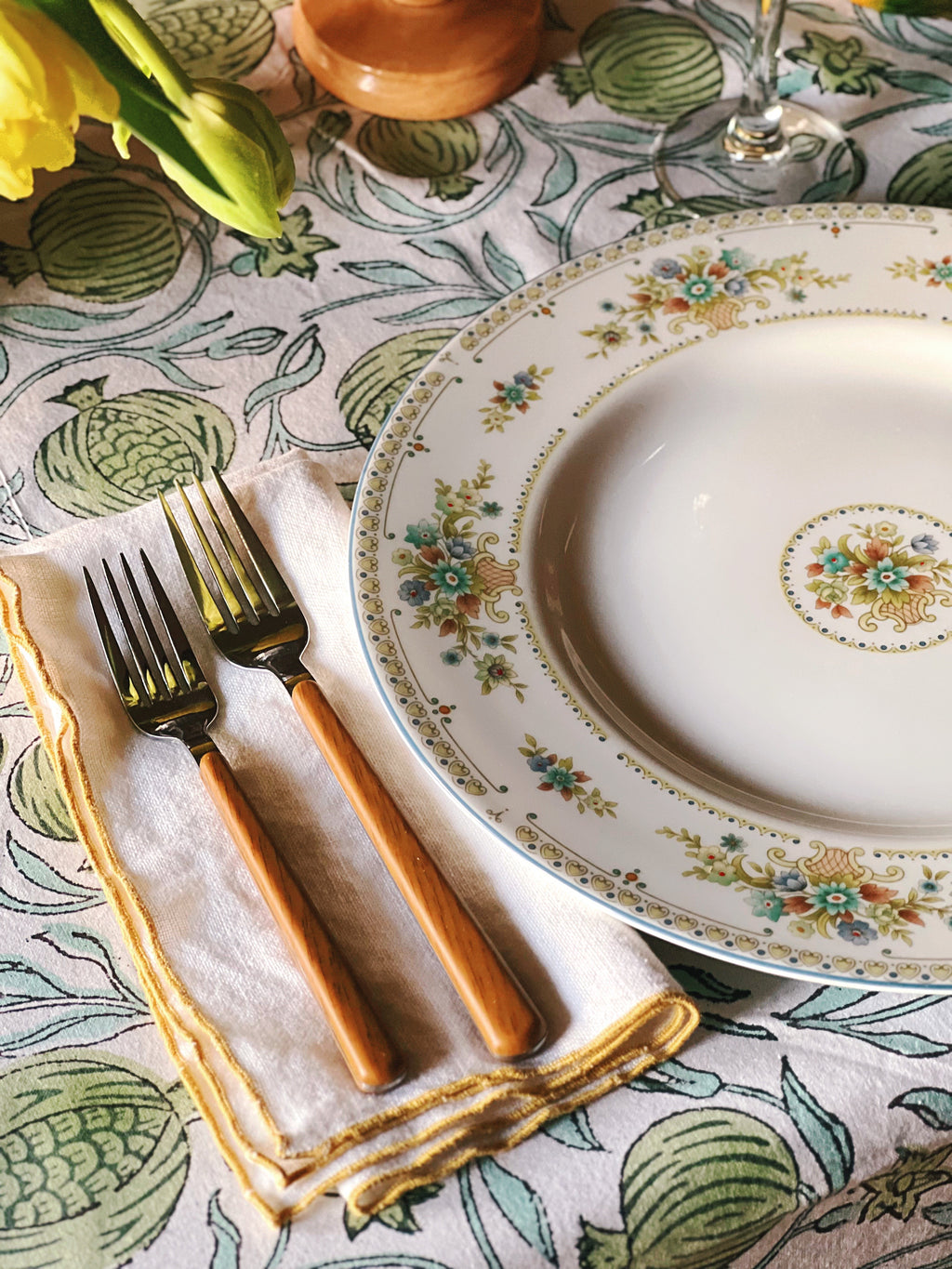 Decorative table setting with a floral plate, silverware, and patterned tablecloth.