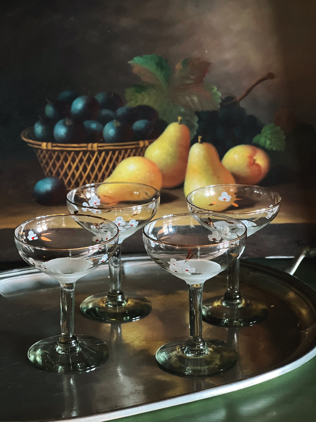 Still life with glasses, pears, and plums on a reflective surface.