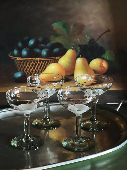 Still life with glasses, pears, and plums on a reflective surface.