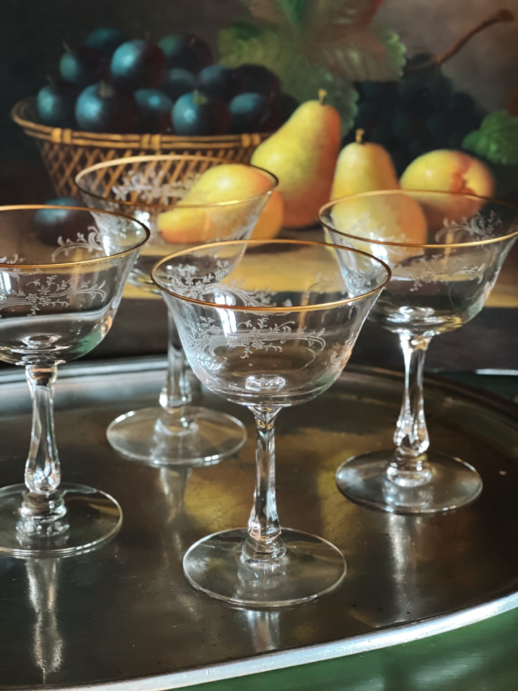 Set of decorative glassware on a reflective surface with fruits in the background