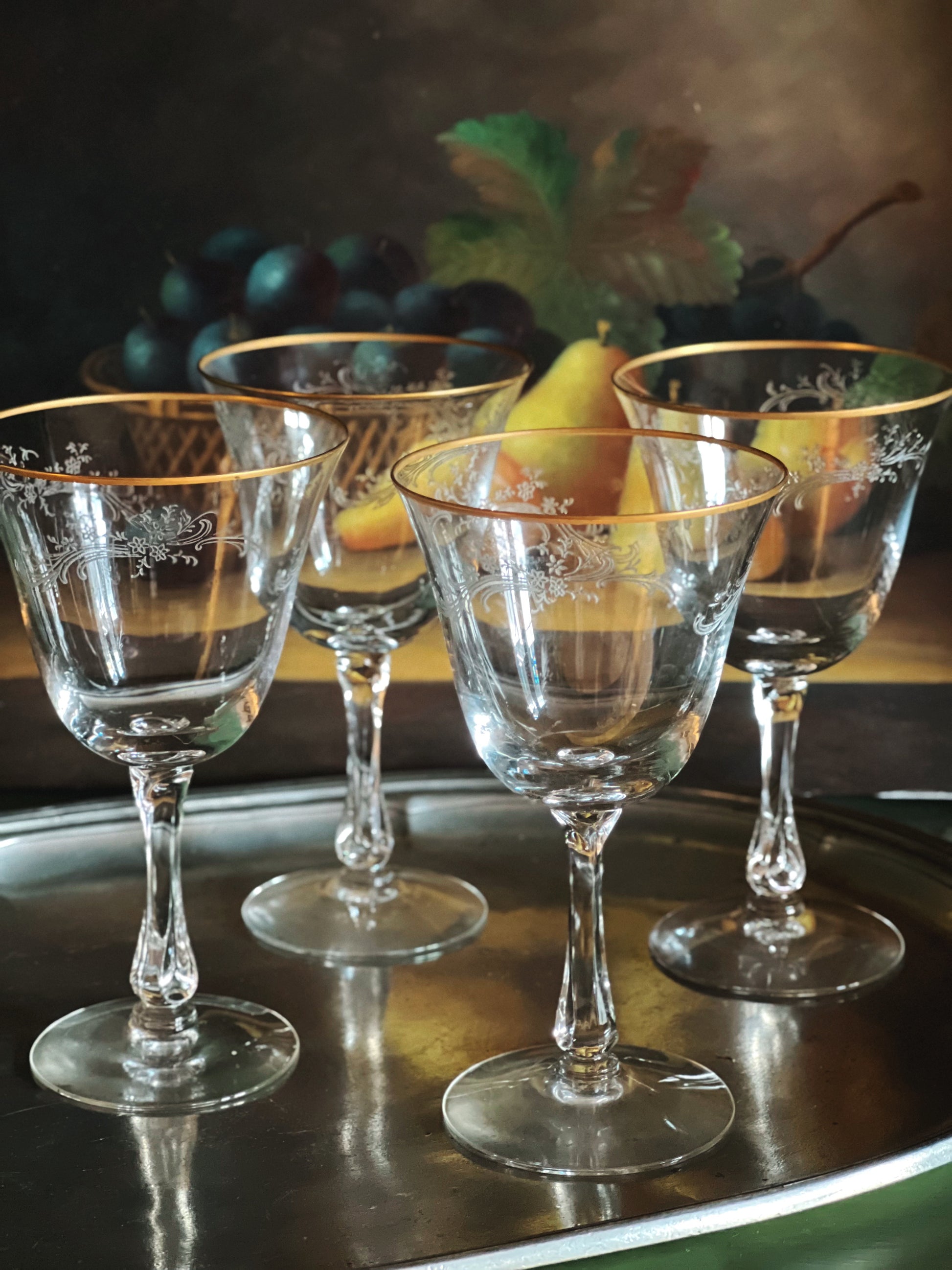 Set of four clear glass goblets with gold rims on a reflective surface.