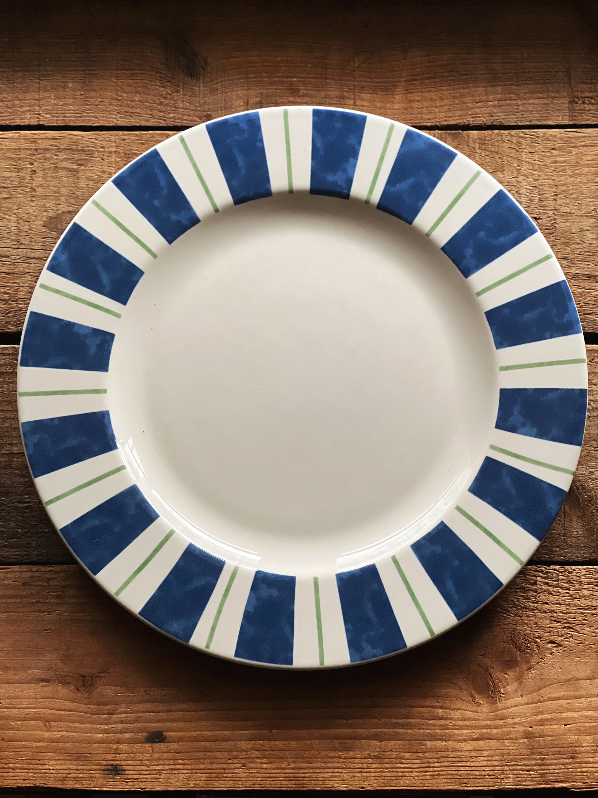 White plate with blue and green striped rim on a wooden surface