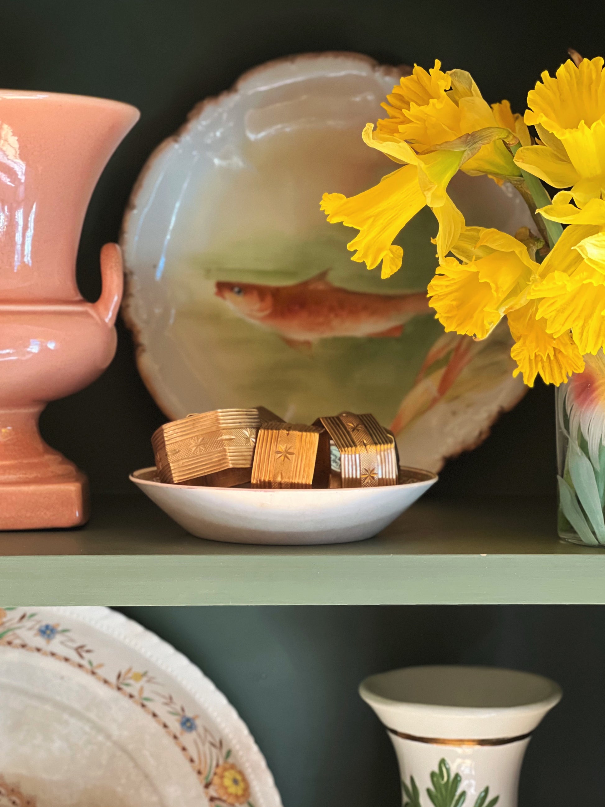 Decorative shelf with ceramic items, a fish bowl, and yellow flowers.