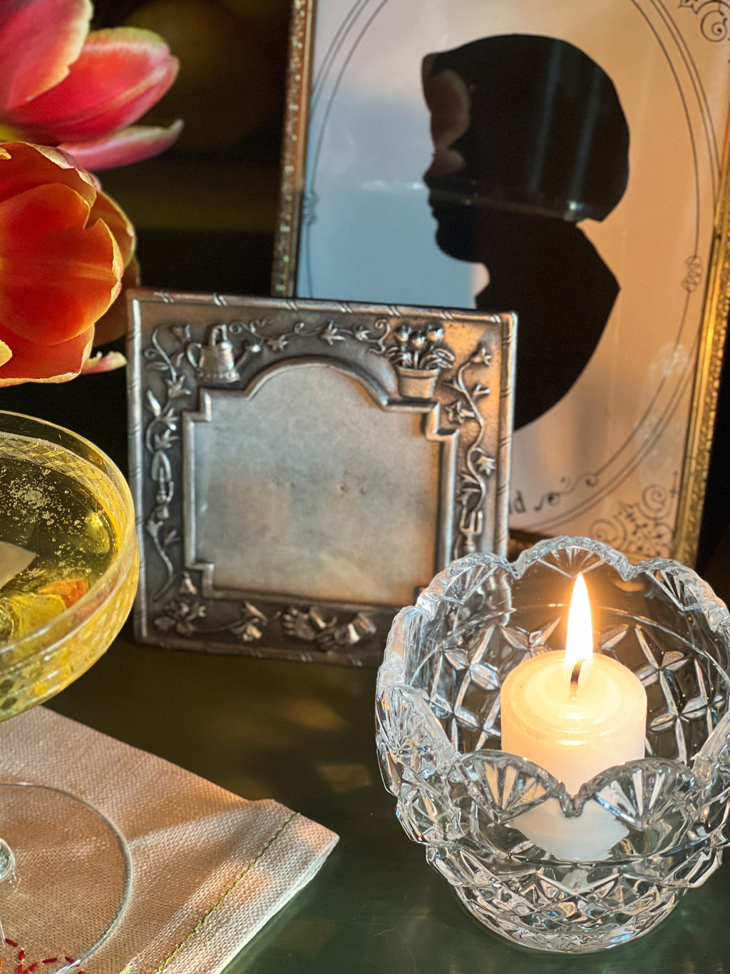 Candle in a crystal holder with a decorative frame and flowers in the background