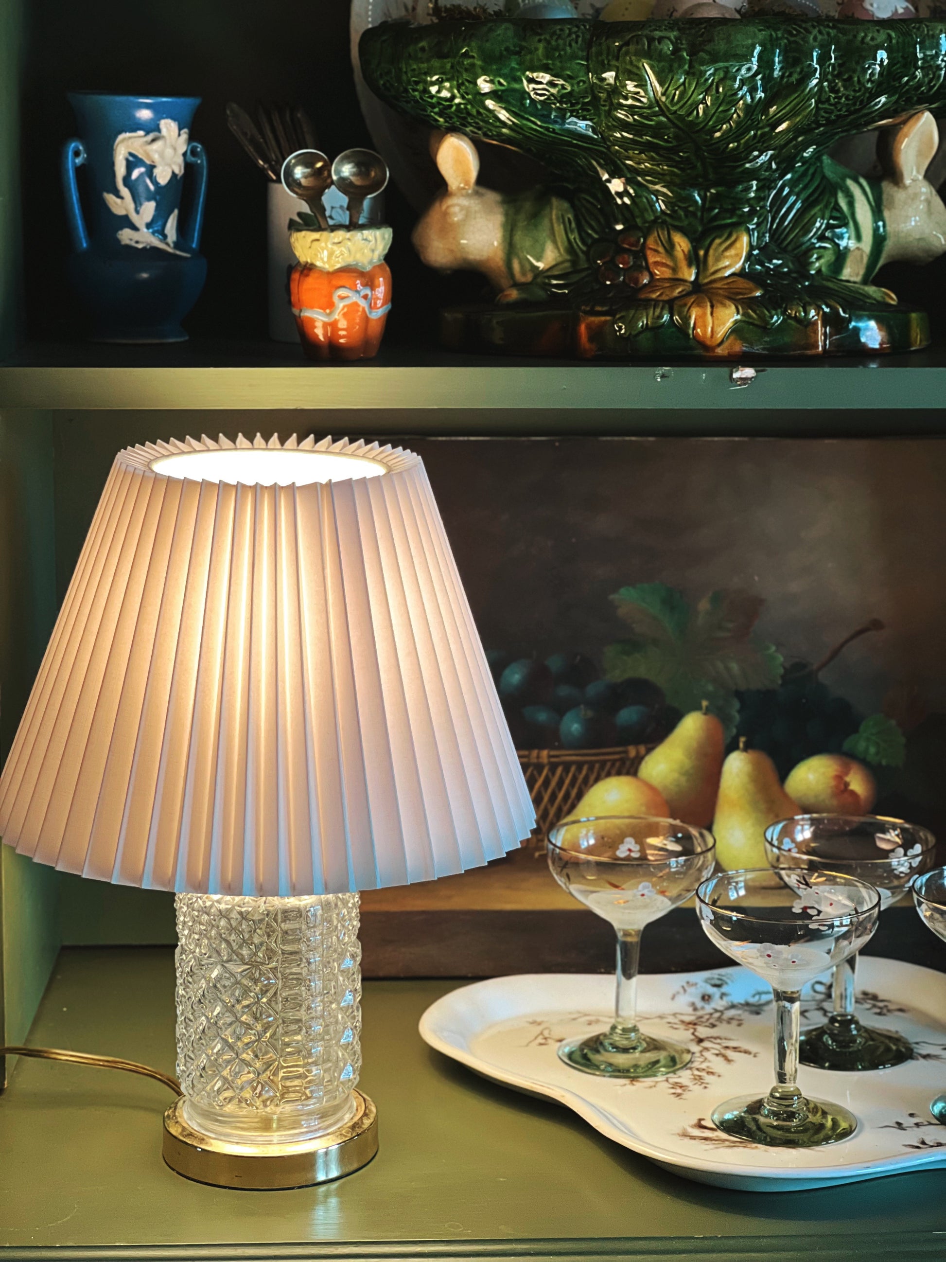 Decorative lamp on a shelf with a painting and fruit in the background