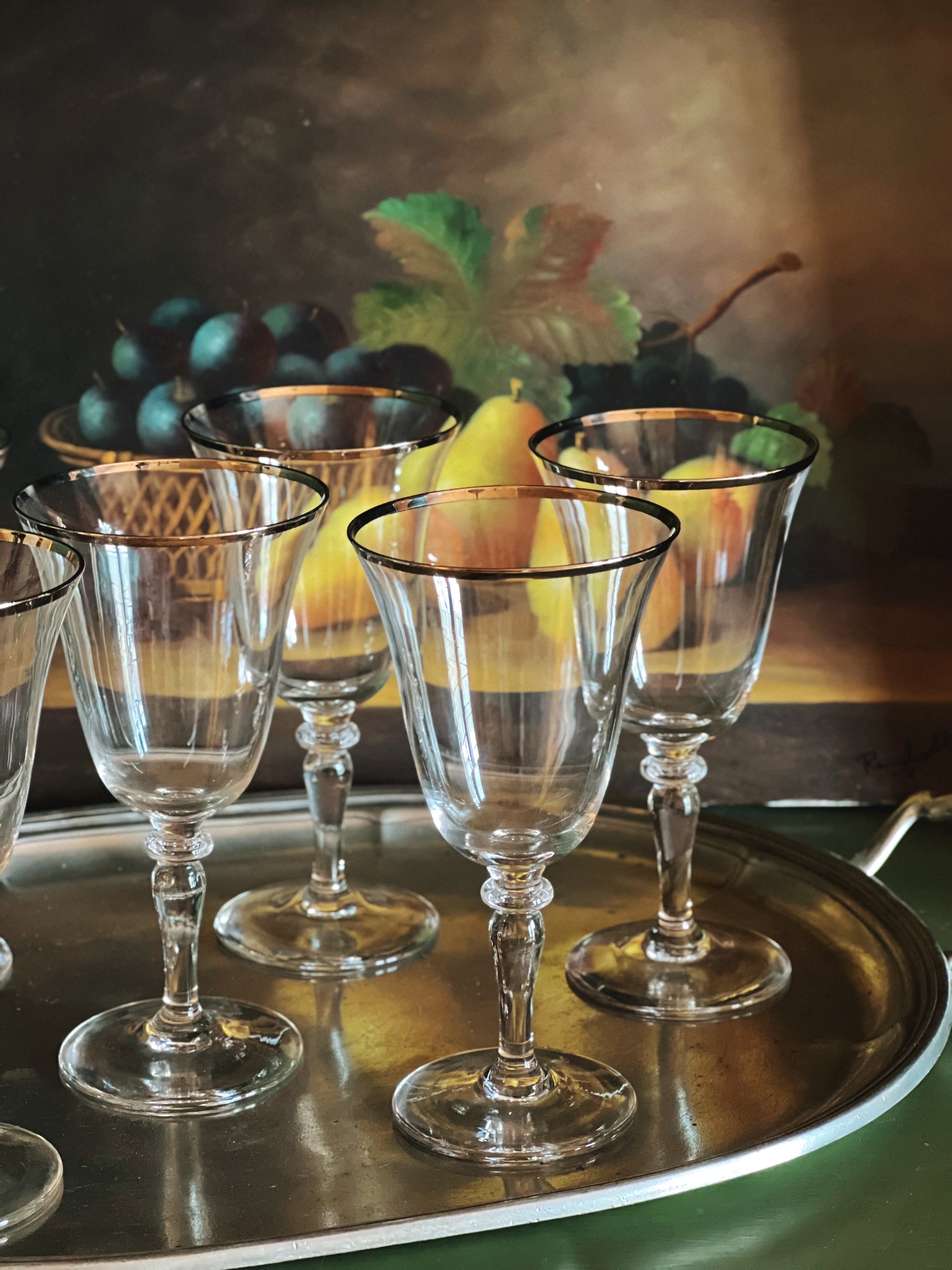 Set of clear wine glasses on a silver tray with a still life painting in the background