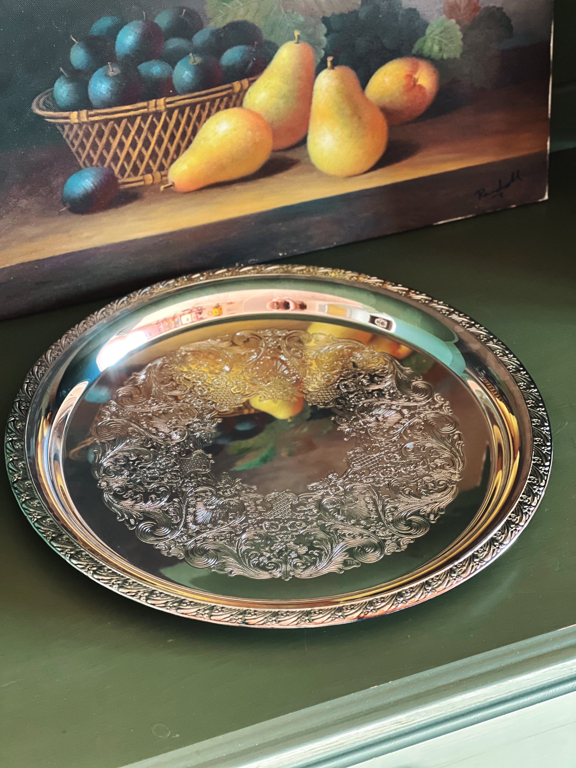 Decorative silver tray with fruit design on a green surface