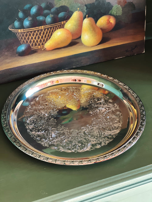 Decorative silver tray with fruit design on a green surface