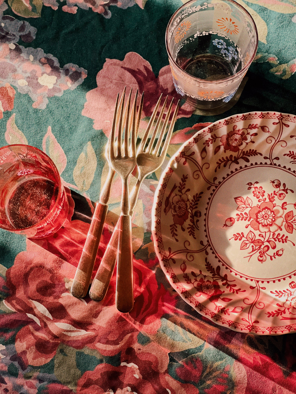 Dinnerware set on a floral tablecloth with a glass of red wine.